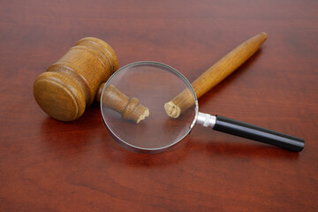 Broken legal system concept. Damaged judge gavel under magnifying glass.