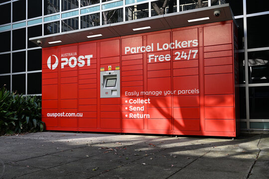 Low shot of red Australia Post 24-7 parcel lockers outside a building at Monash University's Clayton campus, during the day