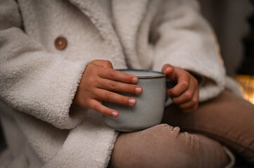 a mug of hot tea in the hands of a girl in a fur coat in nature