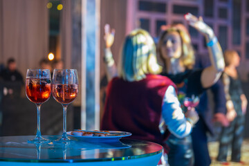 Two glasses of wine on a table in a vibrant party atmosphere with people dancing in the background,...