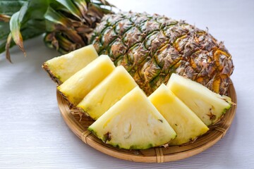 Sliced pineapple in a woven tray on white background