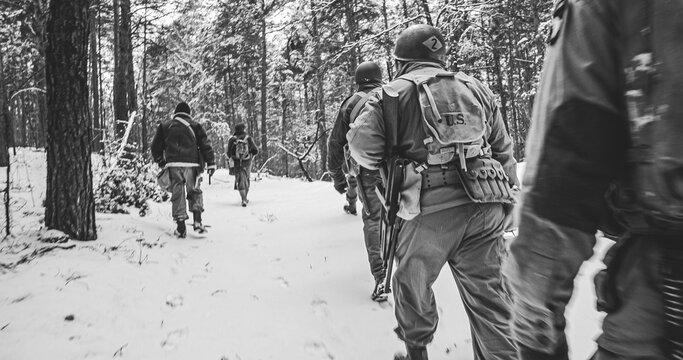 American Infantry Soldier Hard Going Through Forest Road In Cold Winter Day. Squad Usa Soldiers Marching By Country Road. Usa Army Soldiers Of World War Ii. Heroes Of War