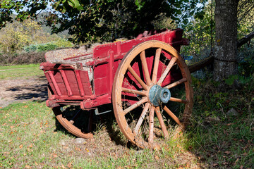 Charrette ou carriole ancienne en bois de couleur rouge avec sa roue cass&eacute;e sous un arbre &agrave; l'entr&eacute;e d'un petit village sur le chemin de randonn&eacute;e d'Apchat dans le puy e D&ocirc;me