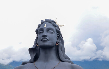  The magnificent sculpture 'Adi Yogi' or Lord Shiva in dark grey shades against the cloudscape at...