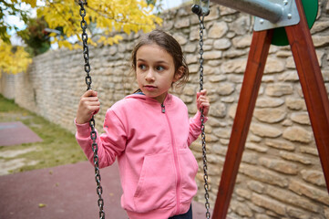 Young girl in pink hoodie enjoying time on playground swing