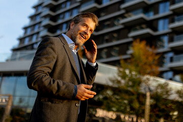 Businessman in smart attire walking while talking on phone in modern urban setting during sunny...