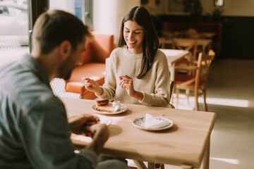 A joyful couple enjoys coffee and pastries in a cozy cafe during a sunny afternoon