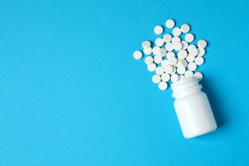 White pills pouring out of a medicine bottle on color background