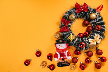 Festive arrangement with a snowman figurine, holiday wreath, and decorations, perfect for Christmas-themed projects on a vibrant orange backdrop.