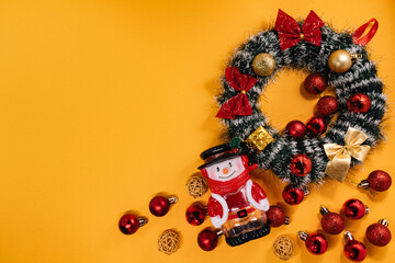Festive arrangement with a snowman figurine, holiday wreath, and decorations, perfect for Christmas-themed projects on a vibrant orange backdrop.