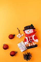Minimalist Christmas composition with a snowman figurine, small red ornaments, and gifts on a bright orange background.
