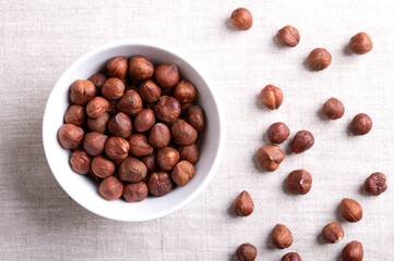 Hazelnut kernels, also known as cobnuts and filberts, in a white bowl on linen. Whole, dried and shelled nuts, fruits of the hazel tree Corylus avellana. Ready to eat as snack, and to use for baking.
