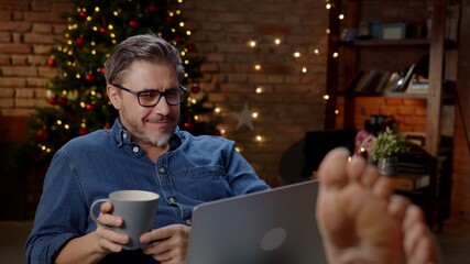 Woman working from home in comfort. Using laptop computer in dark decorated room at home at Christmas in December, Winter.