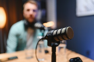 Focus on professional microphone and podcast host in background