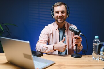 Man podcaster influencer blogger smiling while broadcasting his live audio podcast in studio using...