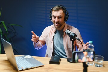A video blogger records content in his studio. The host of the video blog is a young man who is...
