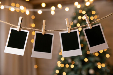 Four blank instant photo frames hanging by wooden clips on a rope, with festive golden bokeh lights and blurred Christmas decorations in the background