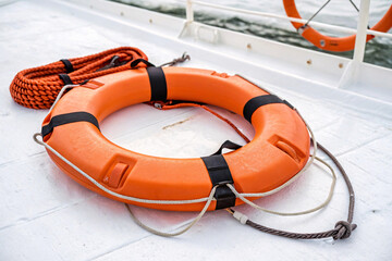 Bright orange life buoy placed on a white deck, tied with ropes, symbolizing safety and readiness during maritime journeys