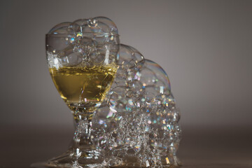 The photo shows soap bubbles floating in the air, creating a dynamic composition. Light through the bubbles creates reflections and a spectrum of colors. An elegant glass, space for text