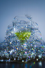 The photo shows soap bubbles floating in the air, creating a dynamic composition. Light through the bubbles creates reflections and a spectrum of colors. An elegant glass, space for text