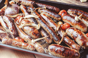 German cuisine. Grill pan with delicious homemade chicken, beef and pork sausages, with mushrooms and tomatoes on the table, close-up