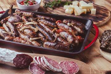 Grill pan with delicious homemade chicken, beef and pork sausages, with mushrooms and tomatoes on a wooden table with ketchup, bread and cheese.