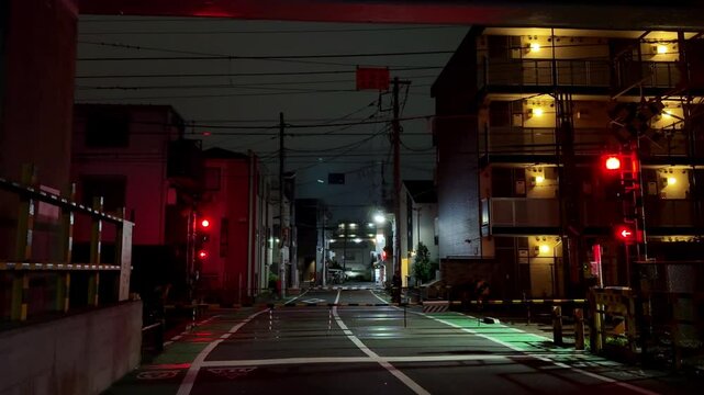 A quiet urban street in Tokyo at night with glowing traffic lights and dimly lit buildings