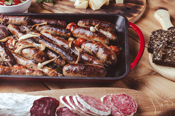 Grill pan with delicious homemade chicken, beef and pork sausages, with mushrooms and tomatoes on a wooden table with ketchup, bread and cheese.
