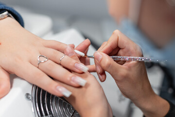 Beautiful girl sits in a beauty salon and gets her nails done. Woman paints nails with a brush and...