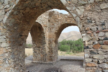 Stone arches in ruins with mountains in the background, symbolizing history amidst nature.