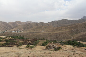 Ancient ruins on a rocky terrain, with a background of distant mountains and cloudy sky.