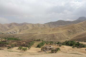 Historical stone structure on dry land with distant mountains under cloudy sky, showcasing ancient heritage.