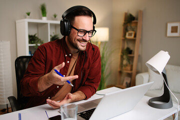 Happy male freelancer wearing headset and speaking during video conference on laptop at home
