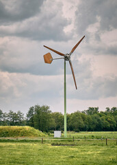Fototapeta premium A rural Dutch landscape featuring a small EAZ wind turbine, green fields, trees, and dramatic clouds on a spring day in the Netherlands.