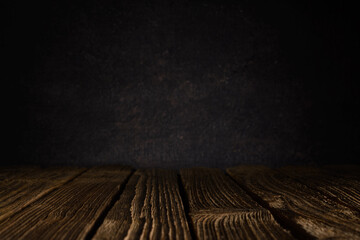 empty wooden table surface made of old textured planks against grey blurred wall with light...