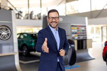 Successful deal in a car showroom, young confident sales man reaching out for a handshake.