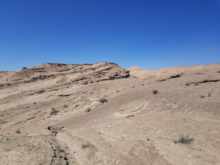 Expansive desert plain with scattered rocks and vegetation, framed by a bright blue sky, ideal for wide landscape and nature photography.