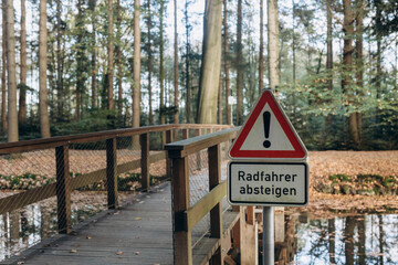 wooden bridge in the forest with a warning road sign that reads 