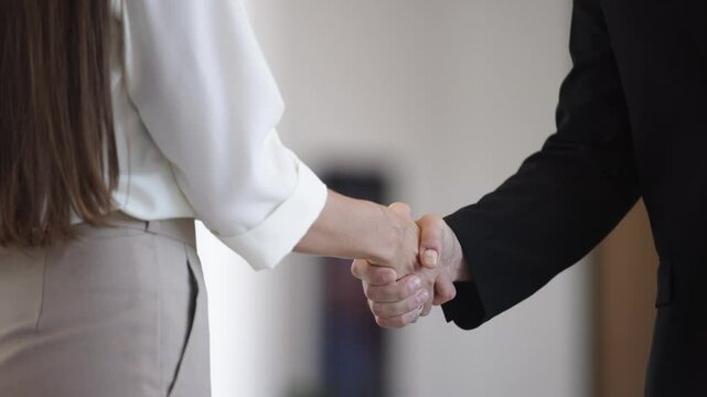 Strong handshake between professionals in corporate environment as symbol of trust and partnership. Close up of handshake between two professionals against background of blurred modern office interior