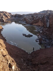 A natural pond surrounded by rocky cliffs, creating a contrast between water and dry terrain, highlighting the beauty of rare oases.