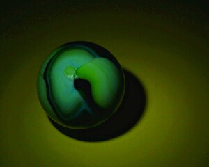 A closeup on a single marble on a dark background and on a yellow table