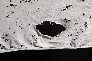 Ragged cloth with holes, grunge damaged white shirt on black background, ripped white fabric with...