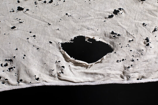 Ragged cloth with holes, grunge damaged white shirt on black background, ripped white fabric with many holes