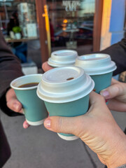 Close up of 4 young people drinking coffee and clinking cups together, symbolizing teamwork, decision making, business, luck, and success