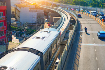 Modern monorail train passes race station on the stage through a tunnel along highway road junction