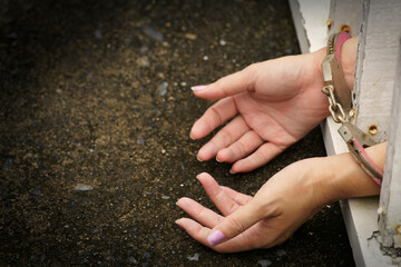 Close-up of a pair of female hands in handcuffs resting on a rough surface, conveying themes of restraint, struggle, and freedom, set against a textured background.