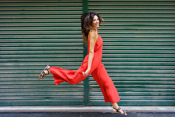 An Energetic Woman Dressed in a Striking Red Dress is Joyfully Walking Outdoors in the City