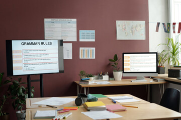 Interactive board with grammar rules standing among desk with desktop computer and wide table in spacious classroom