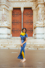 An Indian model in a blue dress and long black hair is posing in front of the Saint-Trophime...