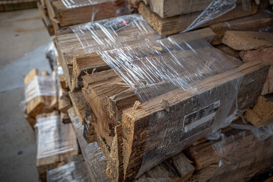 Bundles of kiln dried firewood for home use wrapped in plastic and stacked in a display for sale outside of store.